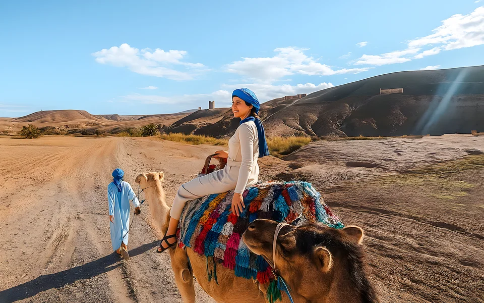 A traveller riding a camel beside rocky desert hills
