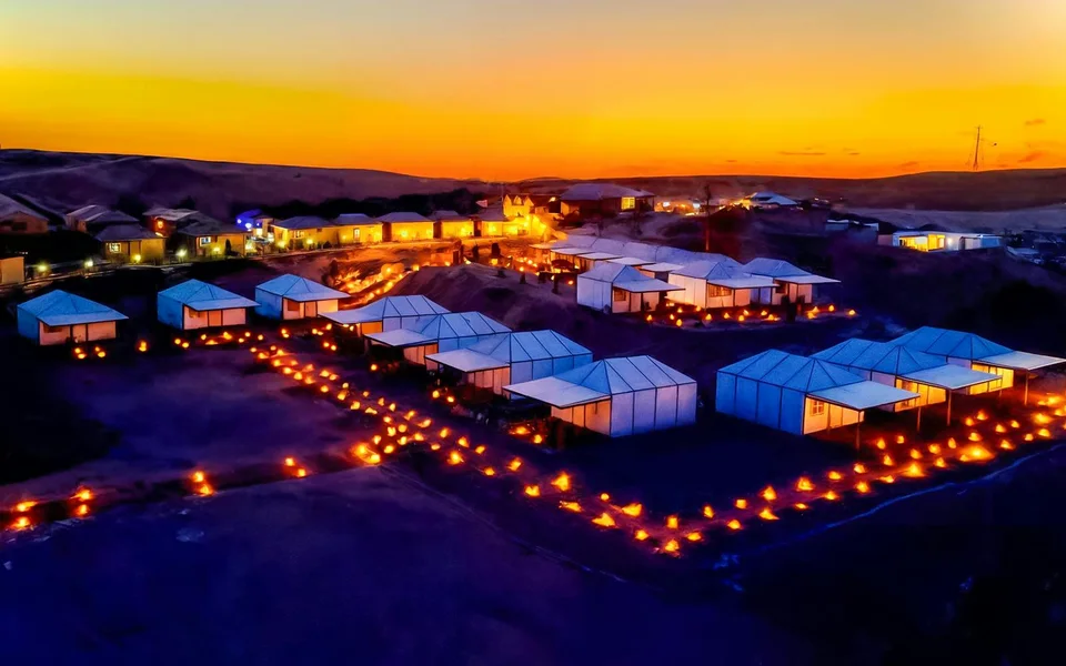 Desert camp tents illuminated beneath an orange evening sky