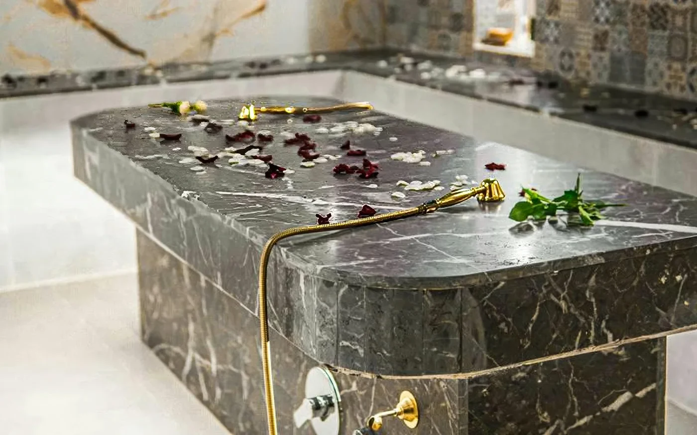 Dark stone treatment platform with petals in a tiled hammam room